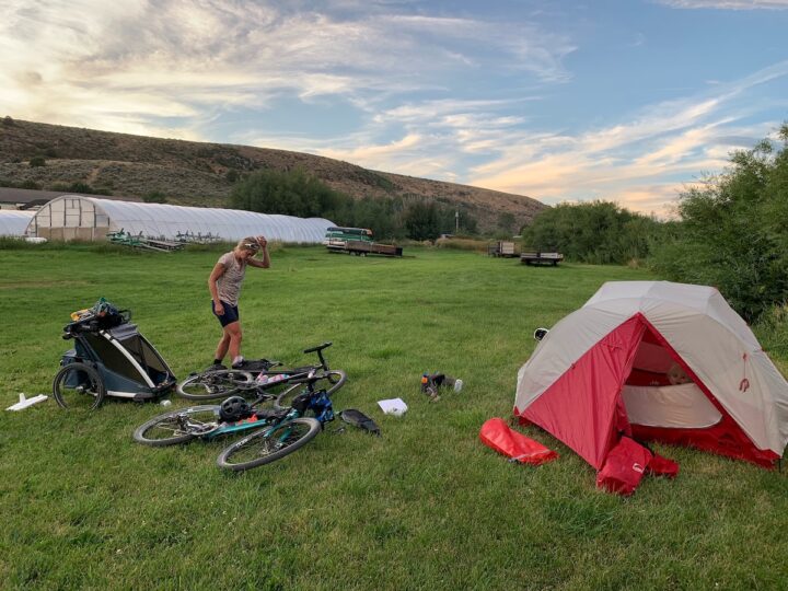 Campsite with tent, bikes, baby trailer, and camp gear scattered around.