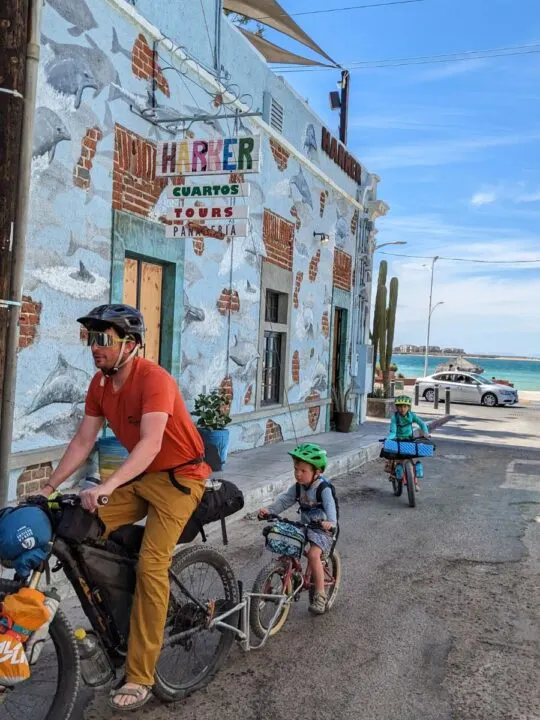 A family rides together using a follow me tandem on a colorful coastal city street.