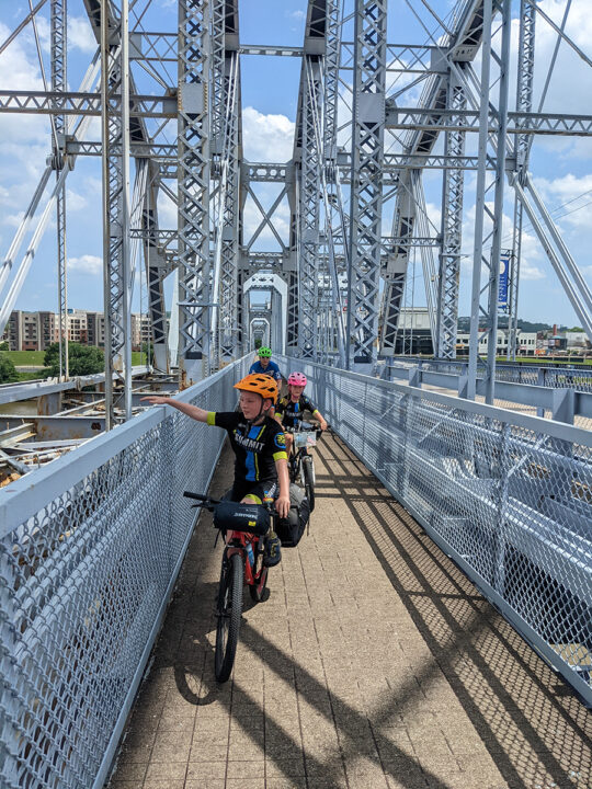 Three cyclists stopped on the pedestrian walkway of a bridge.