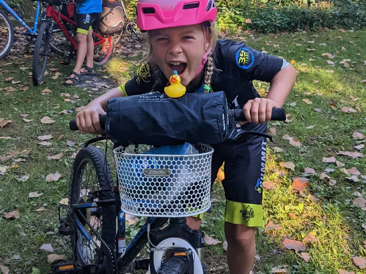 Laughing girl leaning over a rubber duck on her bike handlebars.
