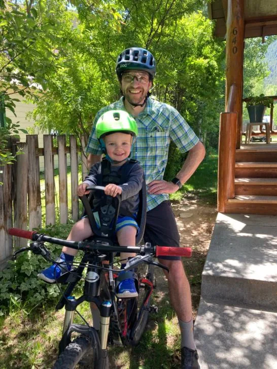 Man standing with mountain bike and toddler riding in a Thule Yepp Mini bike seat