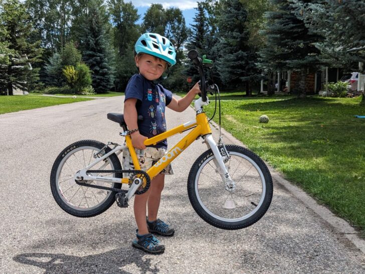 A boy picks up the yellow Woom 16 inch bicycle by himself.