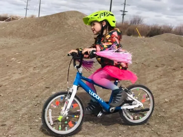 A girl in pink rides a blue Woom 3 on a dirt track.