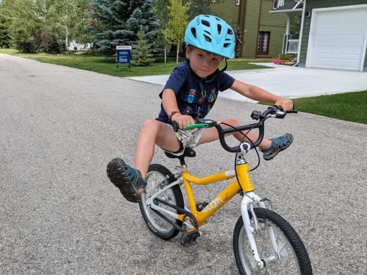 A boy rides a yellow Woom 2 bike with his feet up in the air.