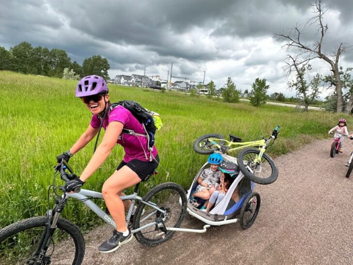 Mom carrying two kids a bike with a flat tire