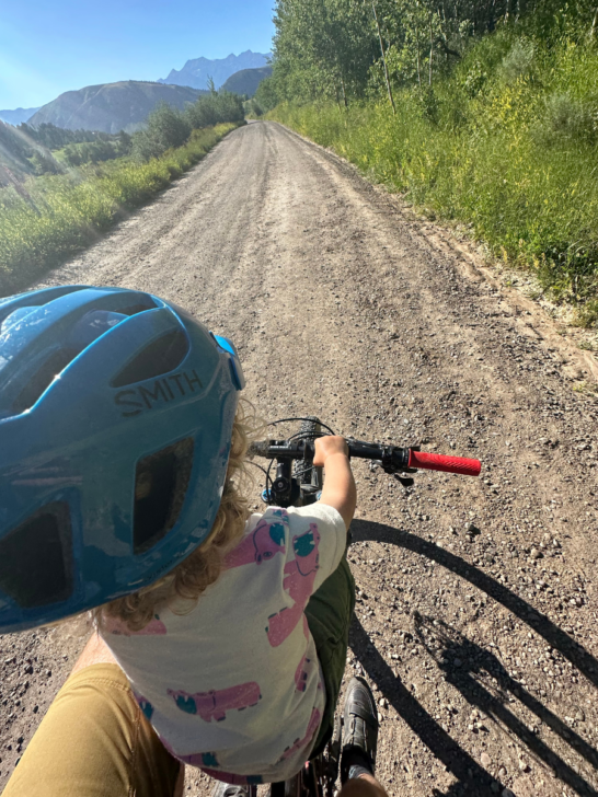 Toddler holds onto mini handlebars while riding on a dirt road.