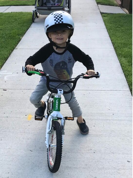 Boy on a green woom 2 bike on a sidewalk.