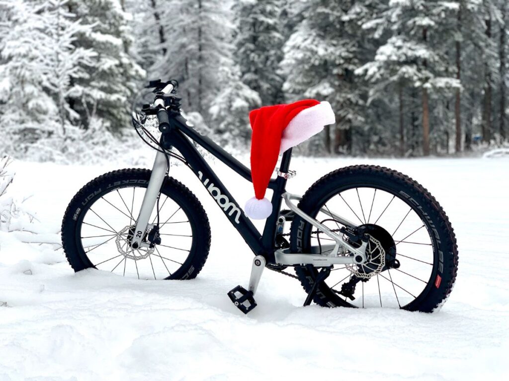 A black Woom mountain bike is propped up in the snow with a santa hat