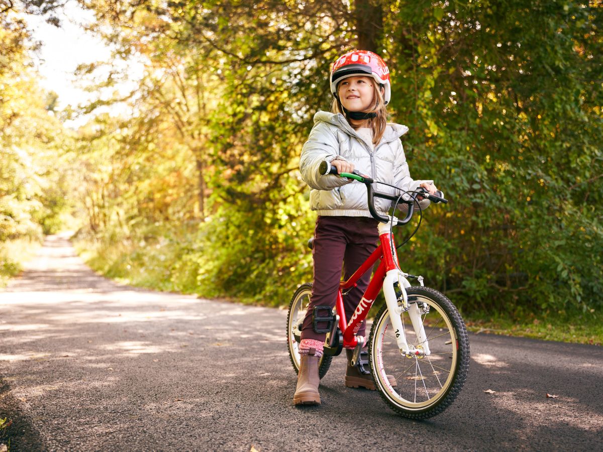 Kid with long hair on red bike and with a red helmet on their head. 