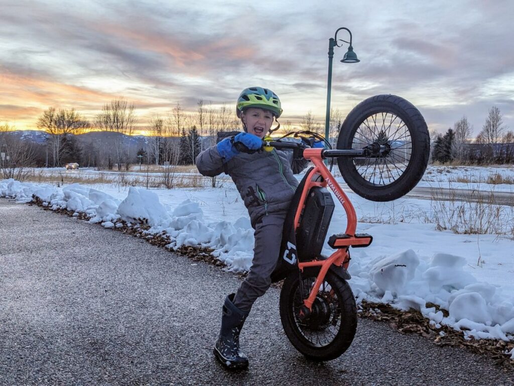 A boy pulls the tire up on his Himiway e-bike in front of the sunset.
