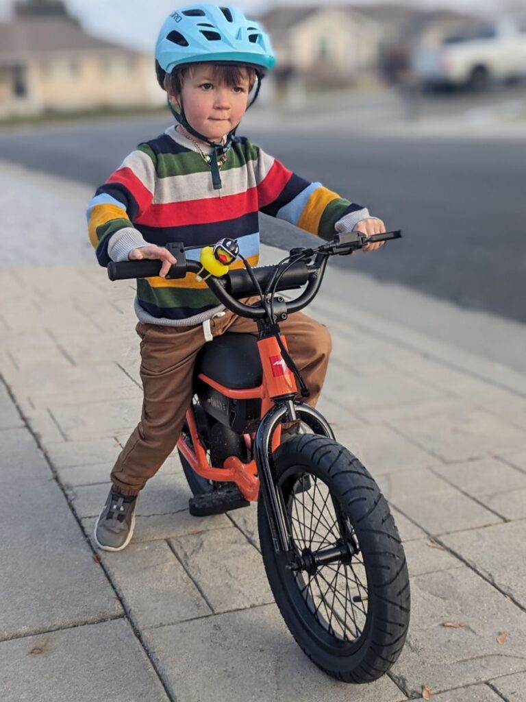 A young boy in a colorful sweater sits atop an orange Himiway kids e-bike.