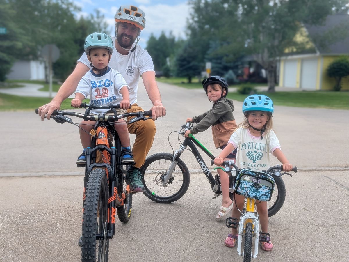 TMM and KRB Horizontal and Featured (36) A dad and three kids pose on bikes on a neighborhood street.